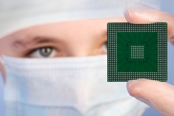 A person in a surgical mask examines a silicon chip