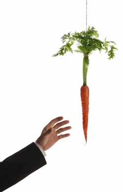 the arm of a person in a suit reaches for a dangling carrot