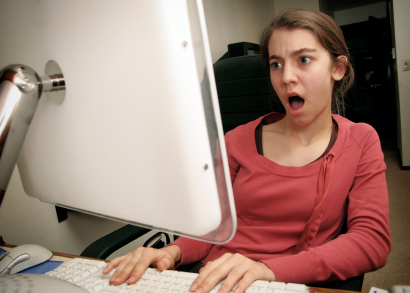 a young woman is shocked by what is on her computer screen