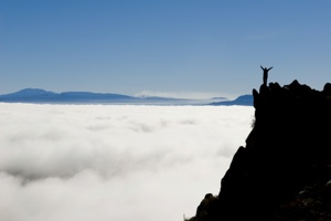 A climber stands at the top of a mountain, above the clouds